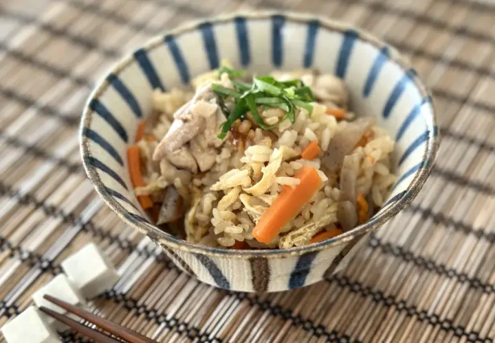 A delicious takikomi gohan recipe served in a striped bowl, featuring rice, chicken, carrots, and green onions.