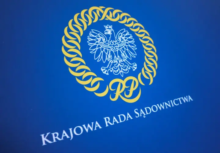 Herb RP i napis "KRAJOWA RADA SĄDOWNICTWA" na niebieskim tle. Symbolika nawiązuje do prawdziwych przyczyn konfliktu wewnątrz KO o zasady powoływania nowej KRS.