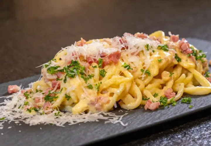 Eine Portion echte Carbonara mit cremiger Sauce, Guanciale und frisch geriebenem Parmesan auf einem dunklen Teller.