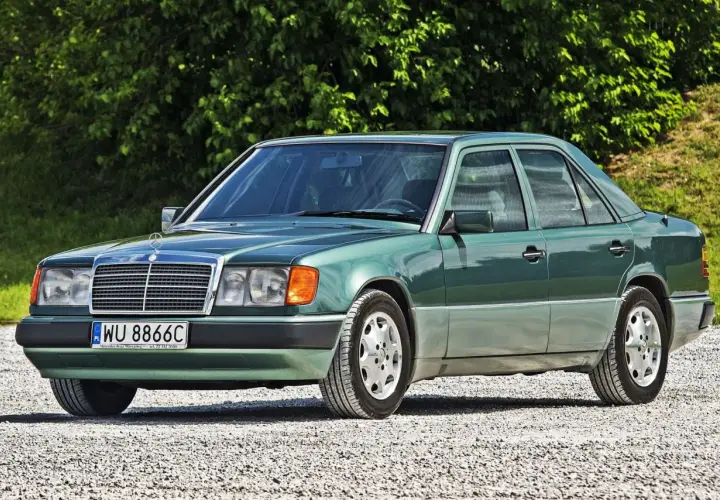 Zielony Mercedes 200 z lat 90. stoi na szutrowej drodze, otoczony zielenią.