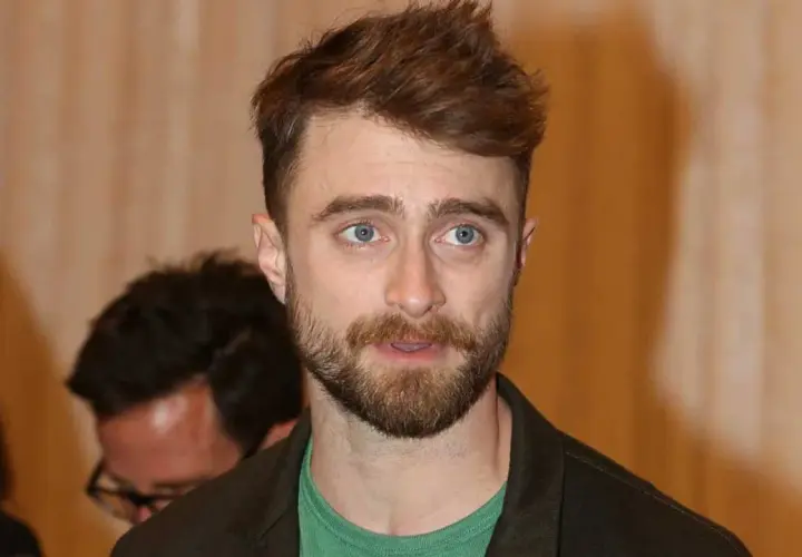 Daniel Radcliffe z zarostem i niebieskimi oczami, jego spojrzenie sugeruje troskę o zdrowie, być może związaną z jego chorobą.