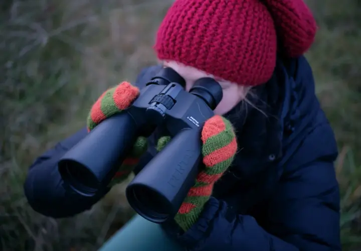 Dziewczyna w czerwonej czapce i rękawiczkach obserwuje niebo przez lornetkę Pentax. Idealna lornetka do obserwacji nieba.