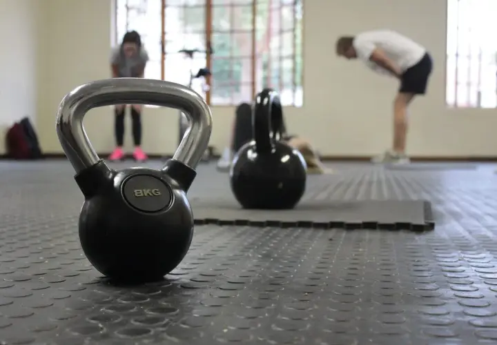 Kettlebell 8kg na siłowni, w tle ćwiczący ludzie.