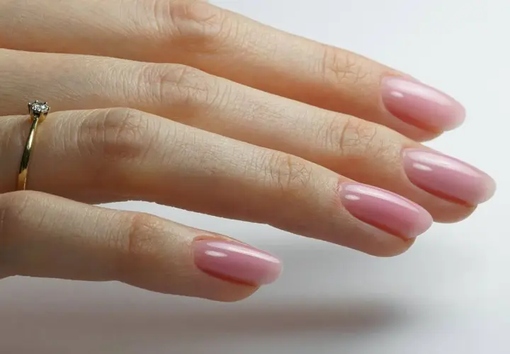 Dłoń z delikatnym, różowym manicurem i pierścionkiem z brylantem. Idealny przykład stylu "clean girl".