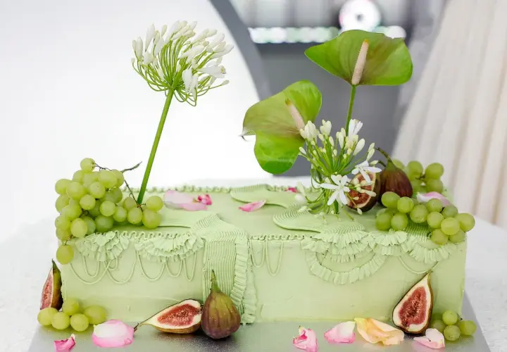 Elegancki tort ślubny w pastelowej zieleni, ozdobiony winogronami, figami i białymi kwiatami.