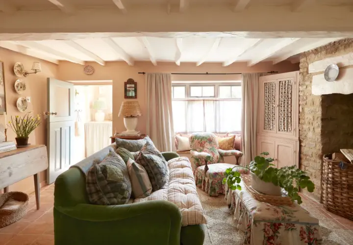 Cozy living room with a green sofa, floral armchair, and charming granny decor. Exposed beams and stone accents add rustic warmth.
