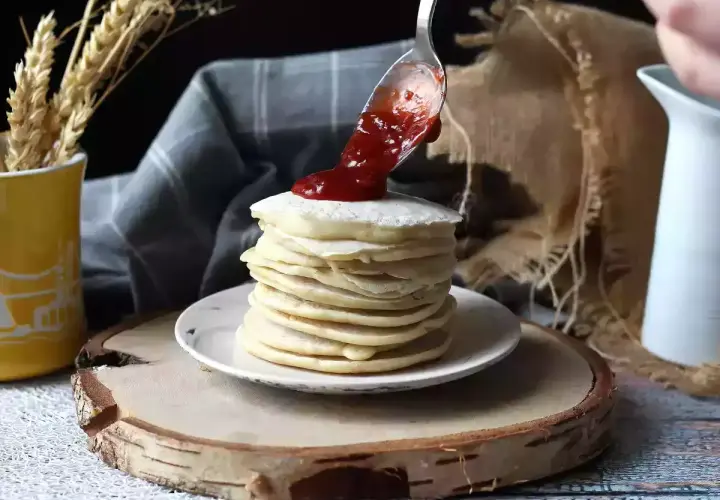 Una cuchara vierte mermelada sobre una pila de tortitas veganas.