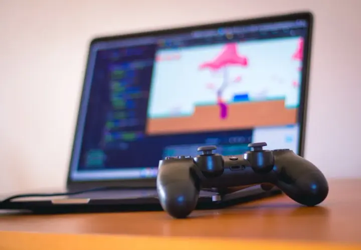 Kontroler PS4 leży przed laptopem z kodem i grą. Dowiedz się, jak podłączyć PS4 do laptopa, by grać na większym ekranie.
