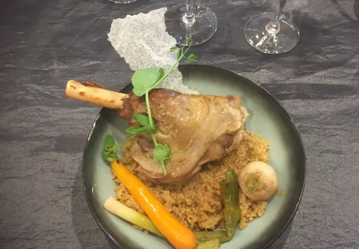 Souris d'agneau braisée au vin, servie sur un lit de couscous avec carottes et navet. Un plat savoureux et réconfortant.