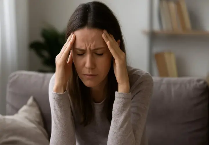 Donna con le mani sulle tempie, occhi chiusi, espressione di profondo stress e possibile esaurimento nervoso.
