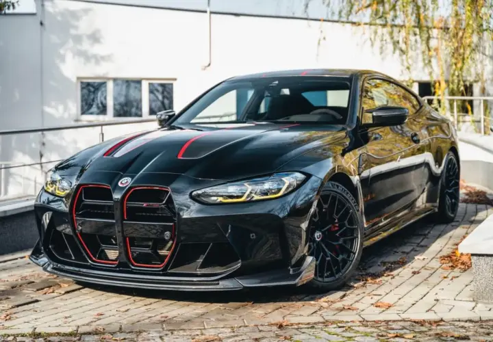 Czarny BMW M4 CSL z czerwonymi akcentami i sportowym dyfuzorem, zaparkowany na bruku.