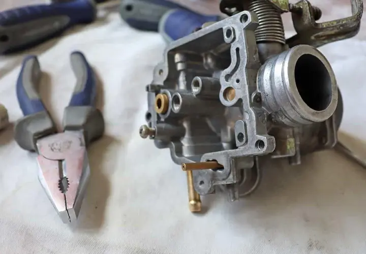 Carburatore smontato, pinze e cacciaviti pronti per la pulizia. Potrebbe essere un modo per risolvere i sintomi di un carburatore sporco.
