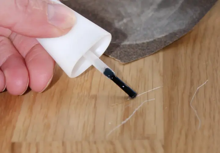Mit einem Lackstift und Schleifpapier kleine Kratzer auf dem Laminat reparieren.