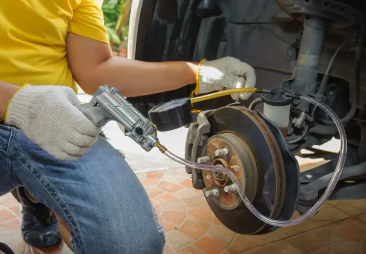 Mechanik w białych rękawiczkach wykonuje odpowietrzanie hamulców przy użyciu specjalnego narzędzia z manometrem.