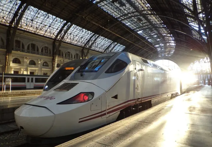 Nowoczesny pociąg Renfe na dworcu, gotowy do podróży z imponującą **tgv prędkość**. Słońce przebija się przez szklany dach.
