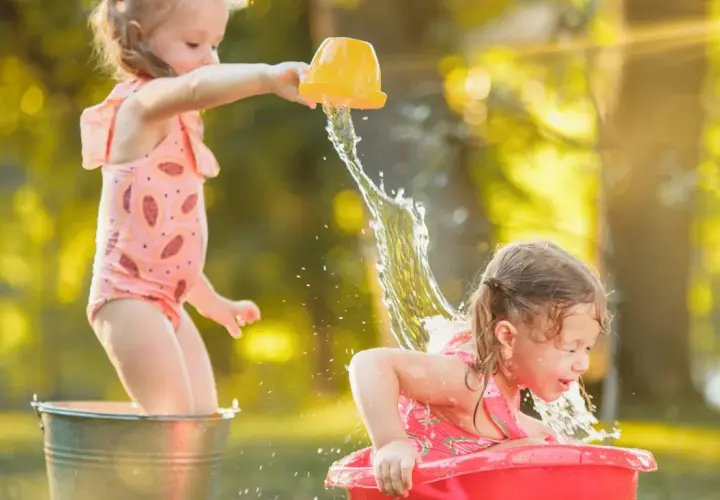 Bambine felici si divertono con giochi d'acqua sotto il sole estivo, spruzzandosi a vicenda con secchielli e bacinelle.