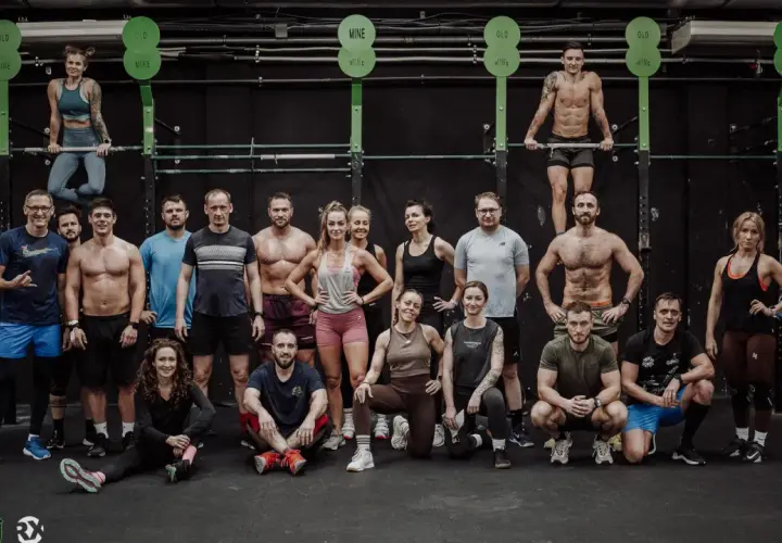 Grupa osób w strojach sportowych pozuje w sali treningowej CrossFit.