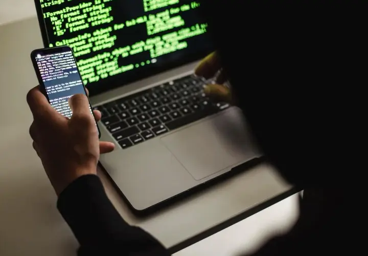 Un développeur web, définition : une personne manipulant du code sur un smartphone et un ordinateur portable, éclairés par la lueur verte des écrans.