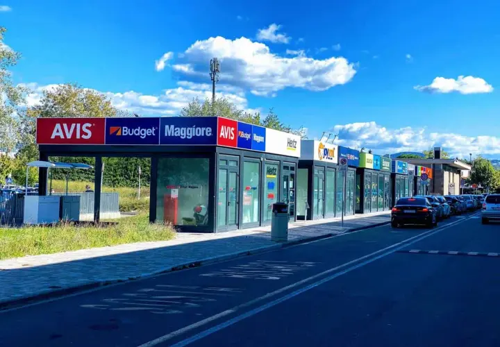 Car rental agencies like Avis, Budget, Maggiore, Hertz, and Europcar line the street, offering options for how to rent a car in Florence, Italy.