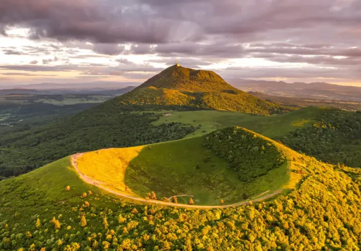 Vue panoramique du Puy de Dôme au coucher du soleil, avec un chemin serpentant sur une colline verdoyante. Idéal pour un séjour en camping-car.