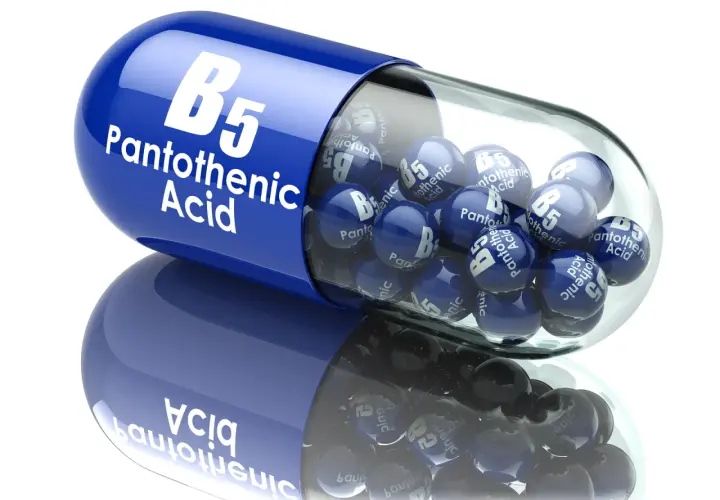 Niebieska kapsułka z napisem "B5 Pantothenic Acid" zawiera małe kuleczki z tym samym oznaczeniem. Witamina B5 w pigułce.