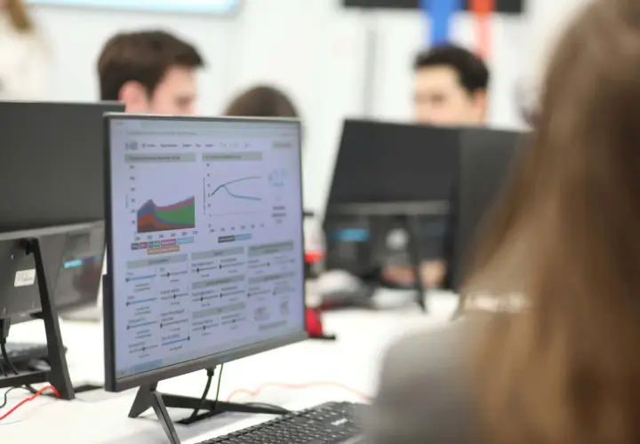 Studenci ekonomiczne analizują wykresy i dane na monitorach, pracując nad projektami.