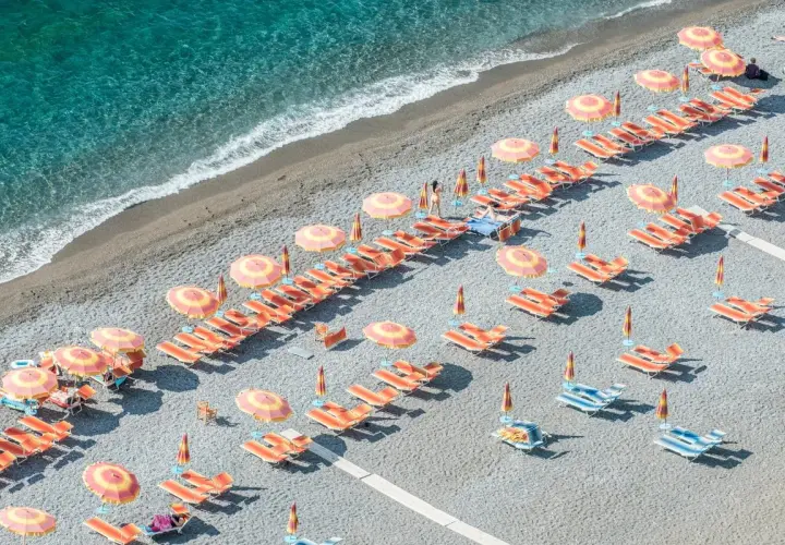 Lignes d'orange vif et de parasols colorés sur une plage de galets, une invitation à la détente. Destination Italie plage.