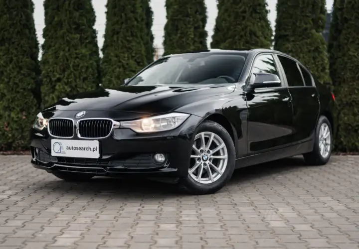 Eleganckie, czarne BMW 318d stoi przed żywopłotem.