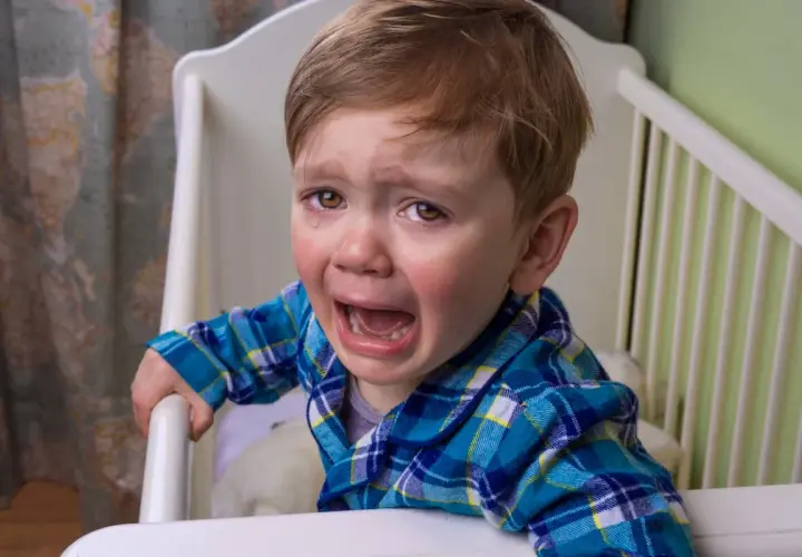 Un niño pequeño con pijama a cuadros llora desconsoladamente en su cuna. Sus ojos están llenos de lágrimas y su boca abierta en un grito.