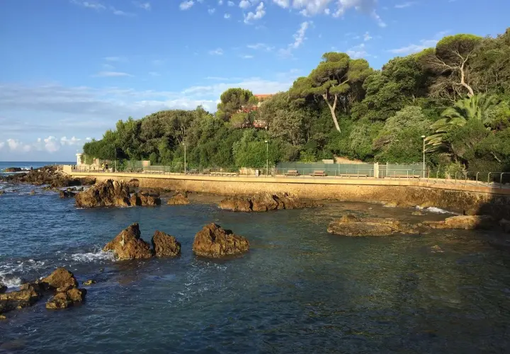 Promenade en bord de mer à Castiglioncello, Italie, avec des rochers dans l'eau et une colline verdoyante.