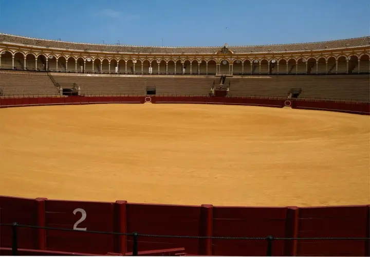 Arena vacía de una de las plazas de primera en España, con gradas y el ruedo de arena dorada bajo un cielo azul.