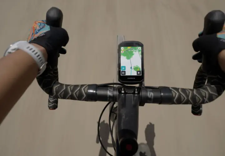 Rowerzysta z rękami w rękawiczkach na kierownicy, na której zamontowany jest Garmin z mapą. Zastanawiasz się, jaki Garmin wybrać?