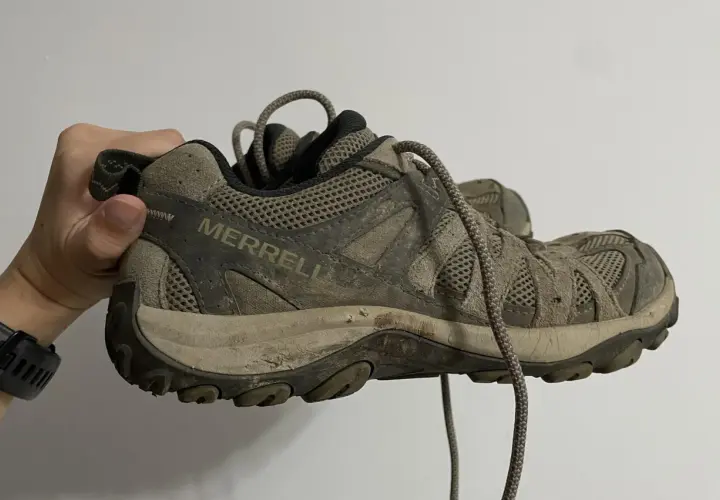 A muddy Merrell hiking shoe is held up, showing its worn tread. This image might inspire ideas on how to rough up the bottom of slippery shoes for better grip.