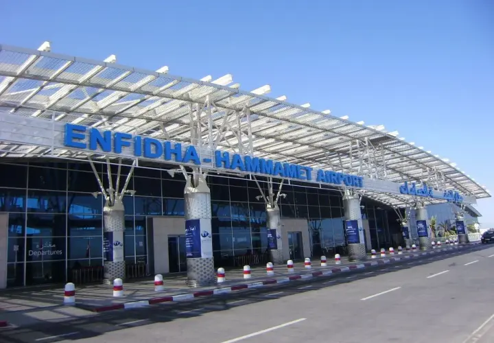 Nowoczesny budynek lotniska Enfidha-Hammamet w Tunezji, z niebieskimi literami nazwy i szklaną fasadą.