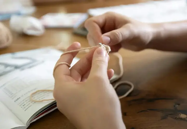 Mani che imparano il lavoro a maglia per principianti, seguendo un libro di istruzioni.