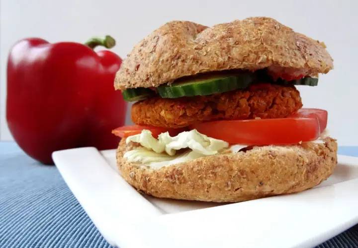 Pyszny burger z ciecierzycy z pomidorem, sałatą i ogórkiem, obok czerwona papryka.