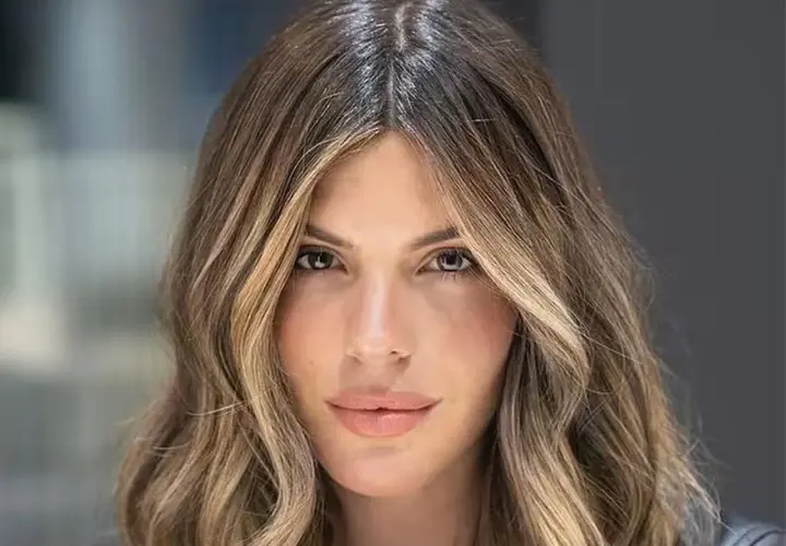 Mujer con pelo castaño con canas y mechas rubias, con ondas suaves y raya en medio.