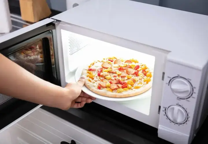 Ręka wkłada mrożoną pizzę do mikrofali. Czy mrożona pizza nadaje się do mikrofali? Zobaczmy!