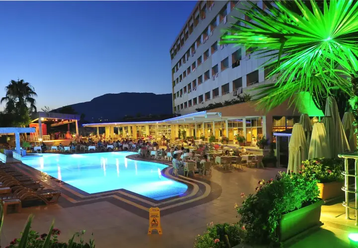 Wieczorny relaks przy basenie w Kirbiyik Resort Hotel. Goście siedzą przy stolikach, a basen lśni błękitem.