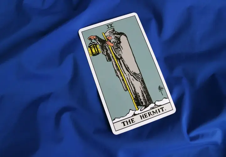 Karta Tarota "Pustelnik" (The Hermit) na niebieskim tle. Symbolizuje introspekcję, mądrość i poszukiwanie wewnętrznego światła.