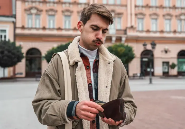 Młody mężczyzna z pustym portfelem w ręku, smutny wyraz twarzy. Inflacja stylu życia dotyka każdego.