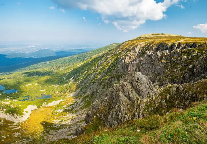 Widok na skaliste zbocze i zieloną dolinę z jeziorami. W oddali widać miasto. To krajobraz, który mógłby być nazwany "śnieżne kotły".