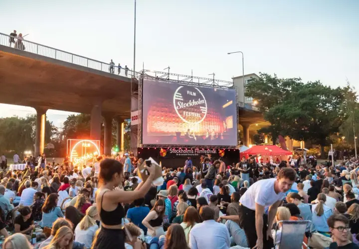 Stor publik samlad för utomhusbio under Stockholms Filmfestival. En stor duk visar festivalens logotyp.