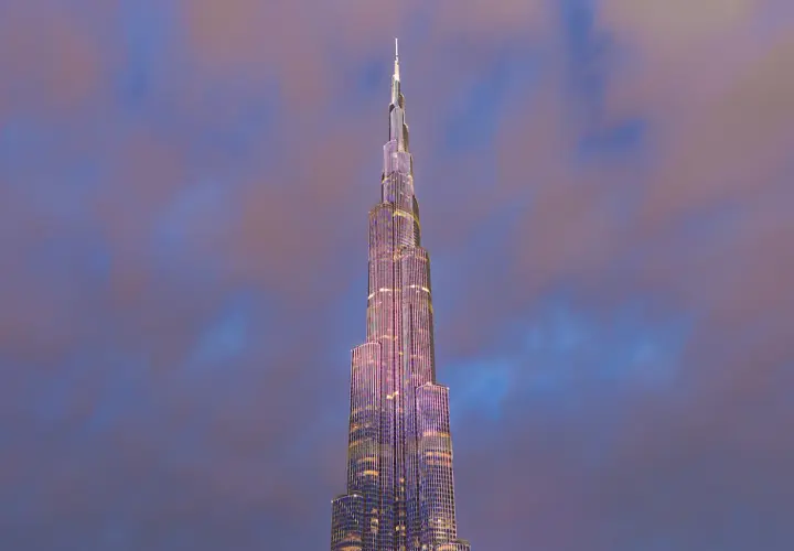 Burj Khalifa oświetlony na fioletowo na tle zachmurzonego nieba.
