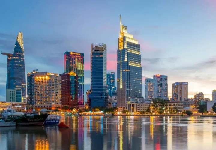 Ho Chi Minh Miasto nocą, z lśniącymi wieżowcami odbijającymi się w wodzie.