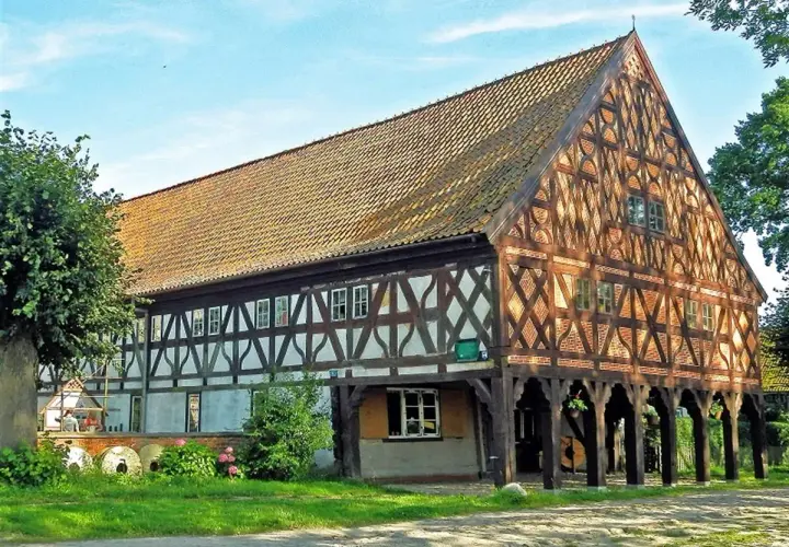 Drewniany dom podcieniowy, część szlaku mennonitów, z charakterystyczną kratownicą i ceramicznym dachem.