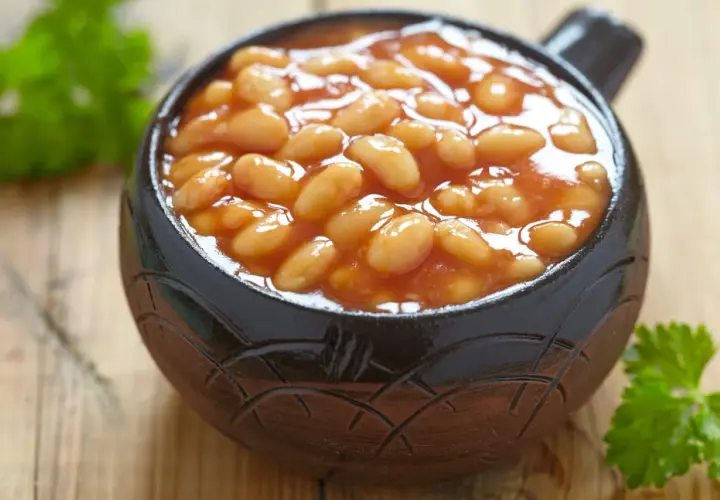 Un bol en terre cuite rempli de haricot blanc en sauce tomate, garni de persil frais sur fond de bois.