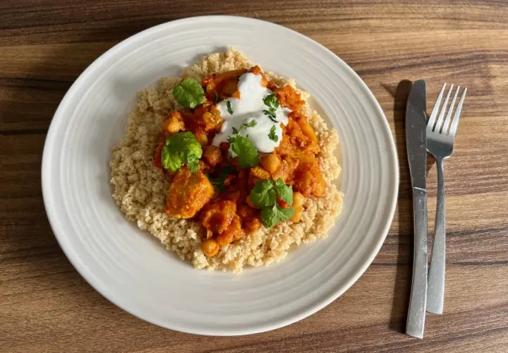 Tagine z kurczakiem i ciecierzycą na kuskusie, udekorowane jogurtem i kolendrą.