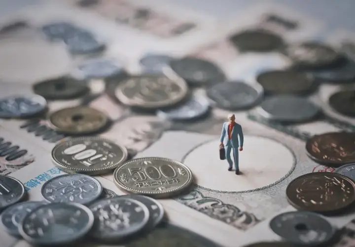 Mała figurka biznesmena stoi na tle japońskich banknotów i monet. To symboliczna wizja krajowej diety i finansów.
