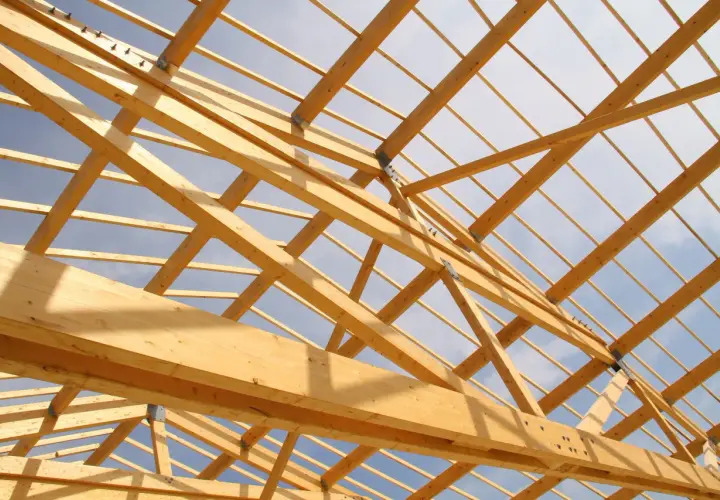 Structure en bois d'une charpente, vue de dessous. Le ciel bleu et nuageux est visible à travers les poutres. Un aperçu pour estimer le prix charpente.